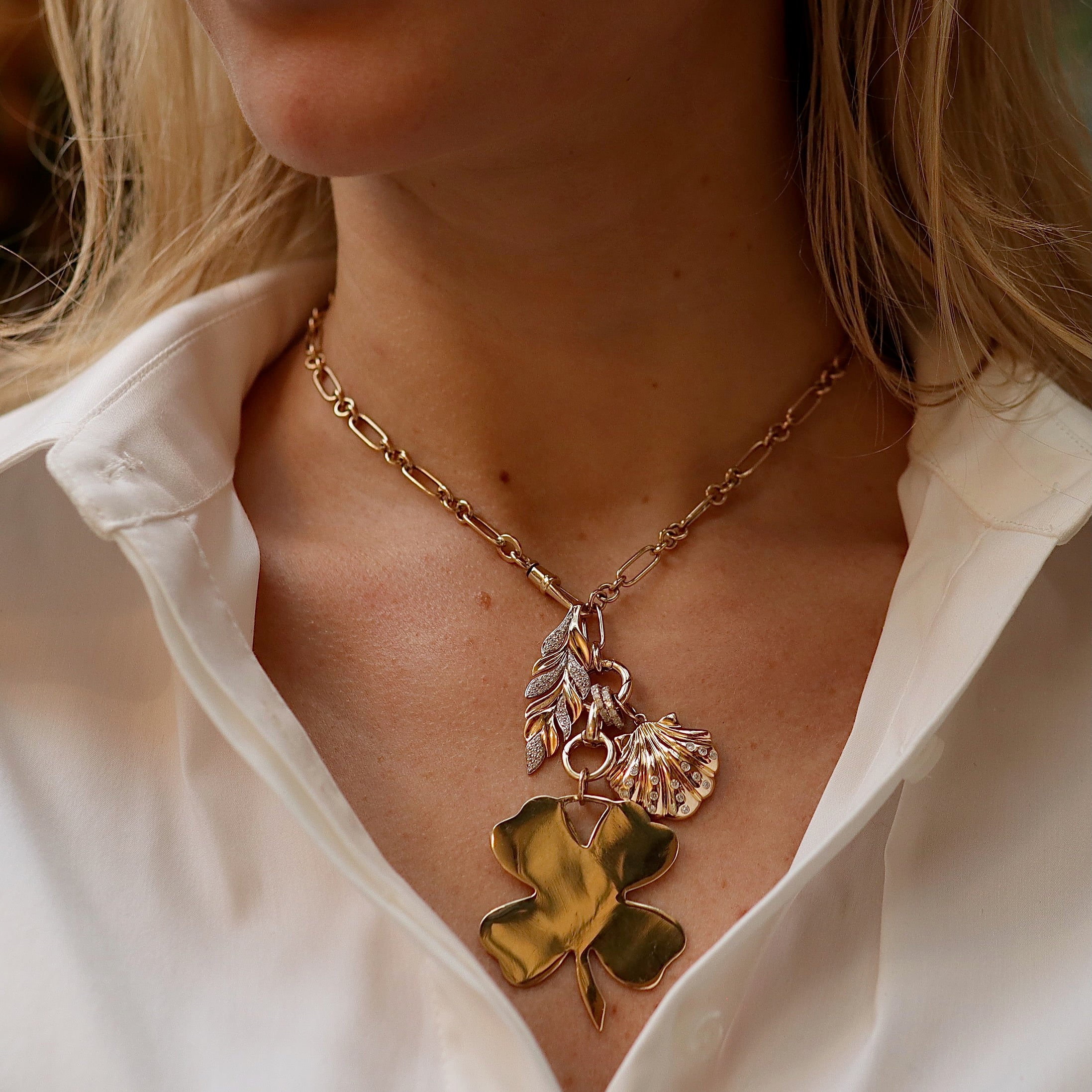Gold necklace with a clover pendant worn by a person in a white shirt.