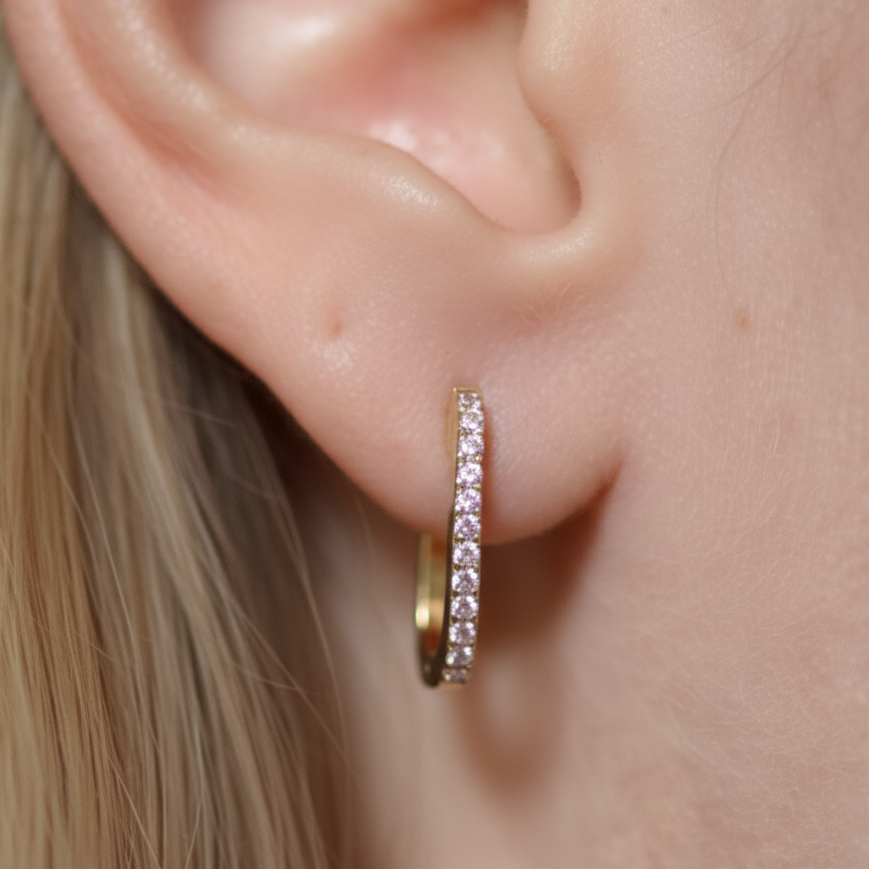 Close-up of a person wearing a 14k yellow gold hoop earring with diamonds.