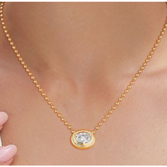 Gold necklace with a diamond pendant worn by a person, blurred background