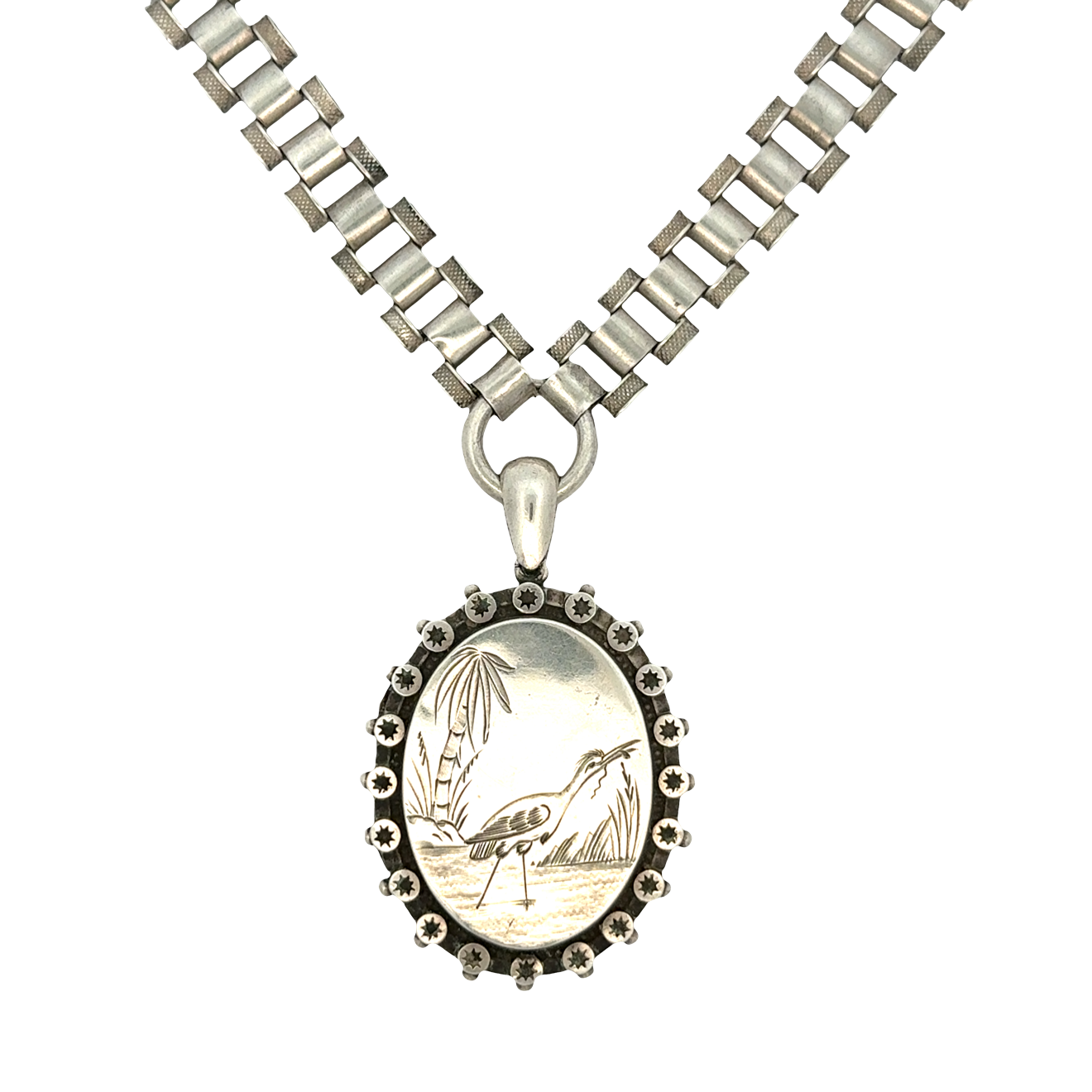 Victorian sterling silver necklace with an oval locket engraved with a heron standing by water and palm trees, framed by starburst accents, on a geometric link chain.