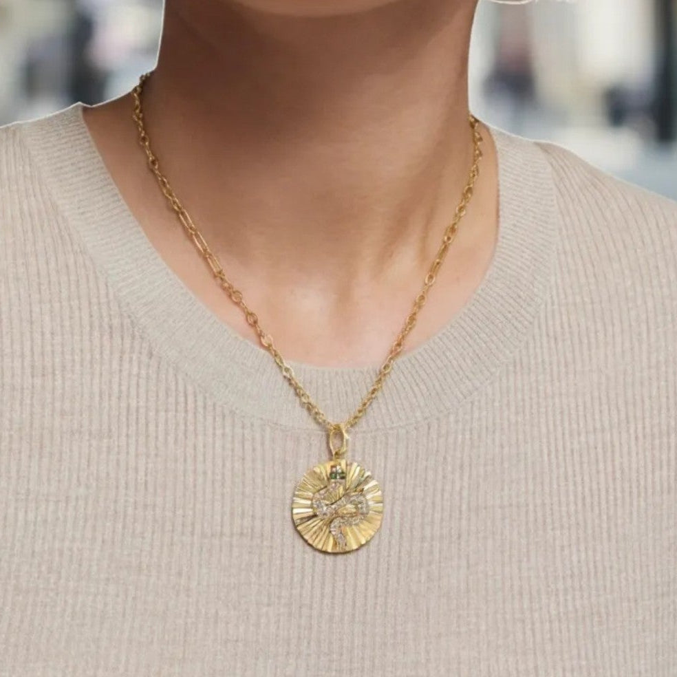 Gold necklace with a pendant worn by a person in a beige sweater.