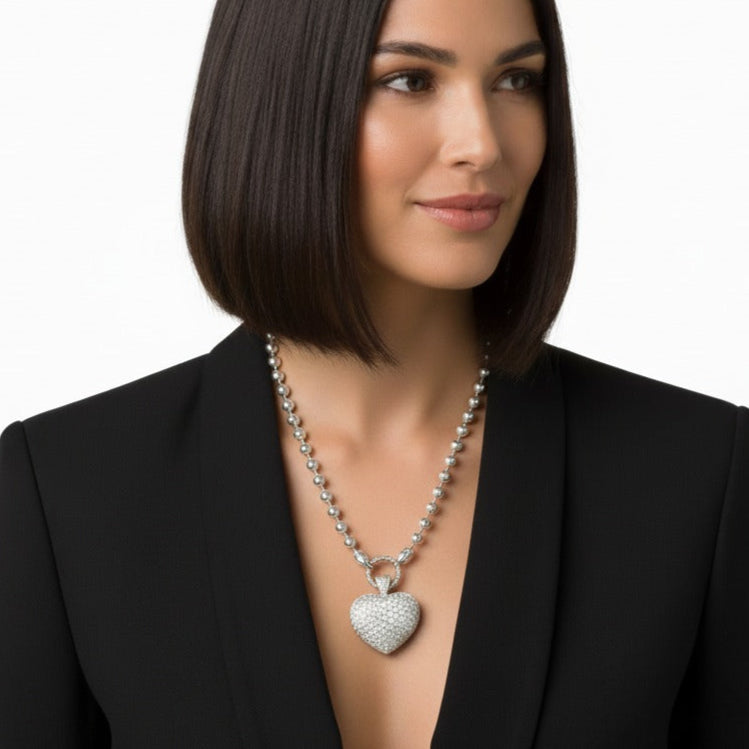Woman wearing a black blazer with a pave heart-shaped pendant on a white background